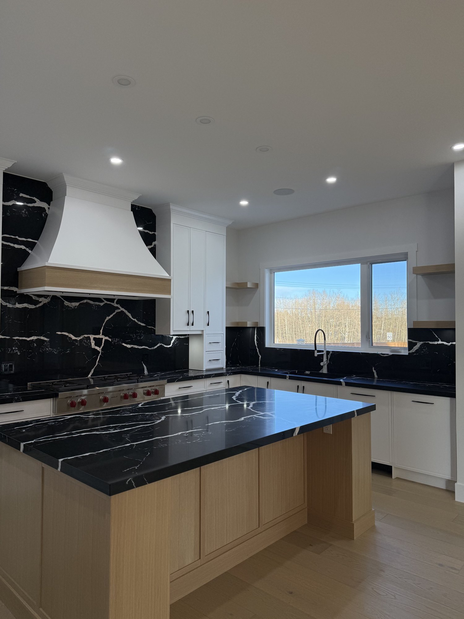 Kitchen with a black marble island and backsplash, an oak base and a white range hood
