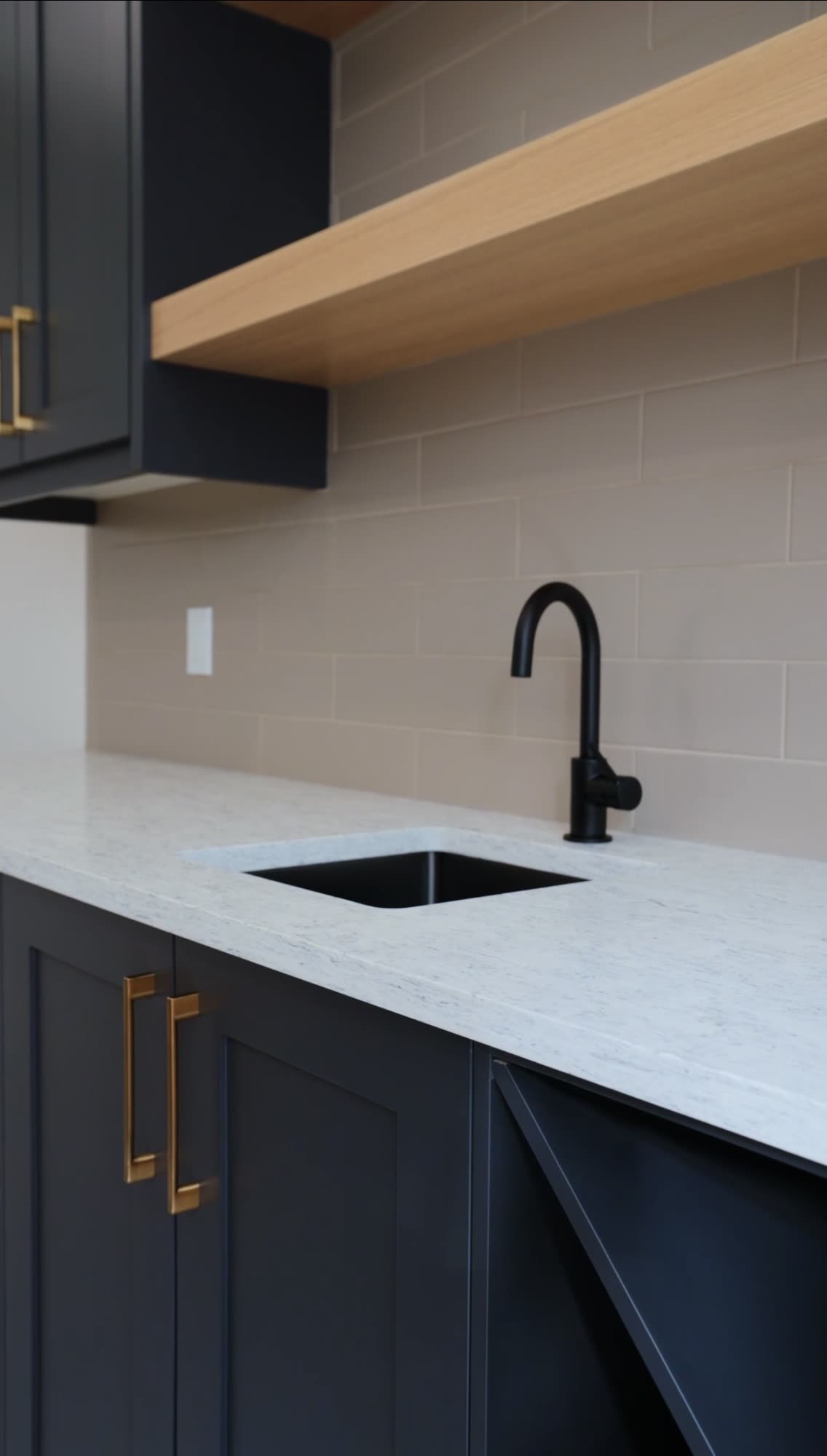 Wet bar with navy cabinetry, an oak floating shelf and a black tap