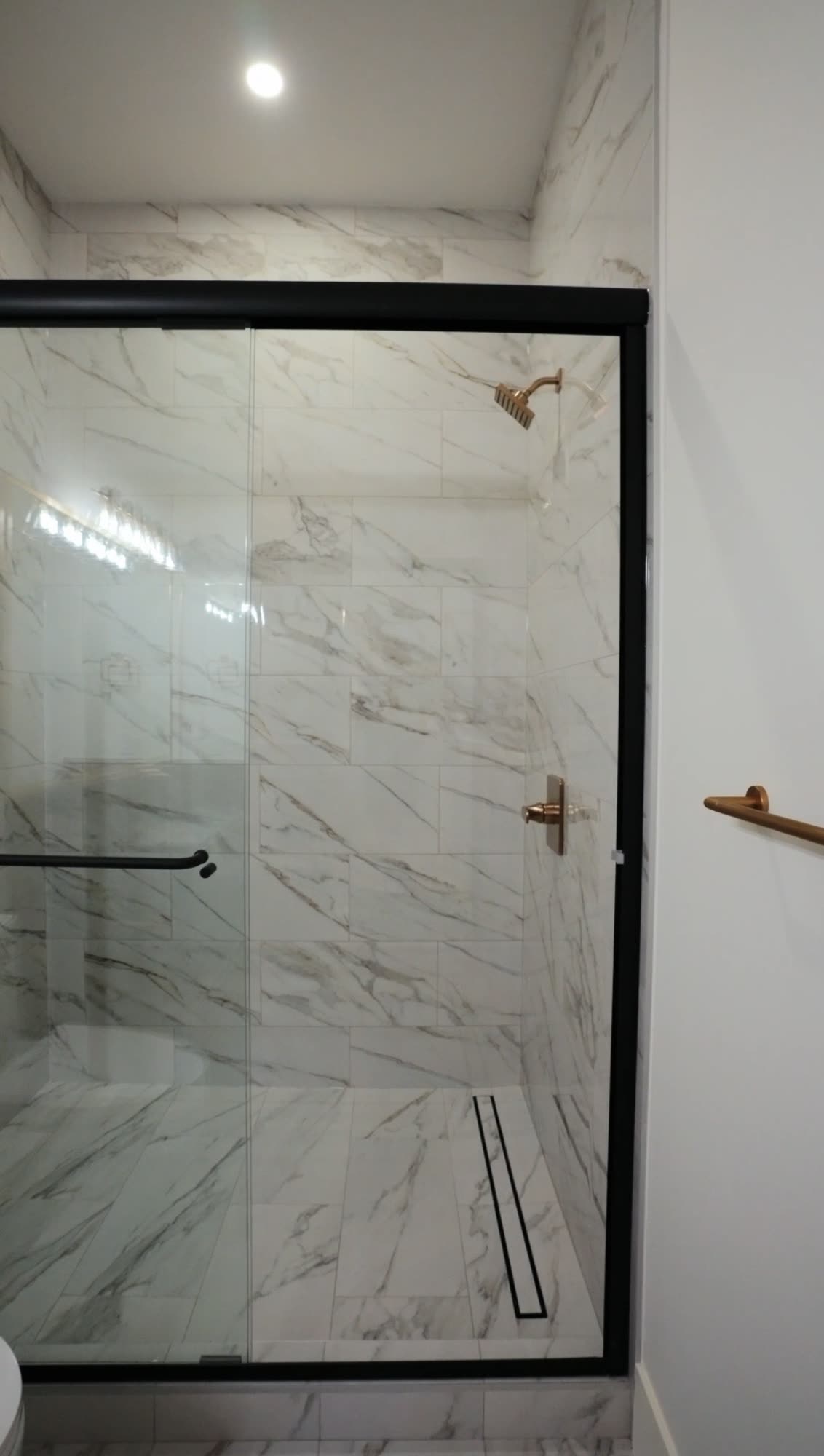 Walk in shower with marble tile, a linear drain and a black framed glass door