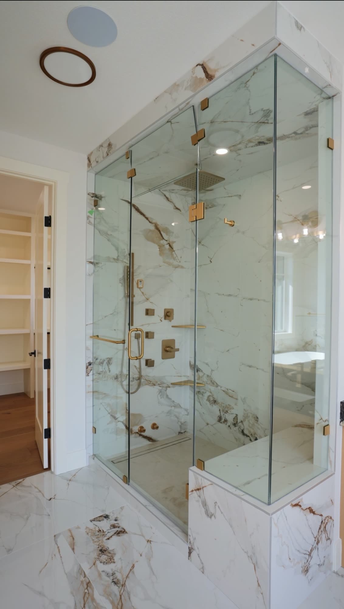 Glass shower enclosure with brass hardware against a marble surround