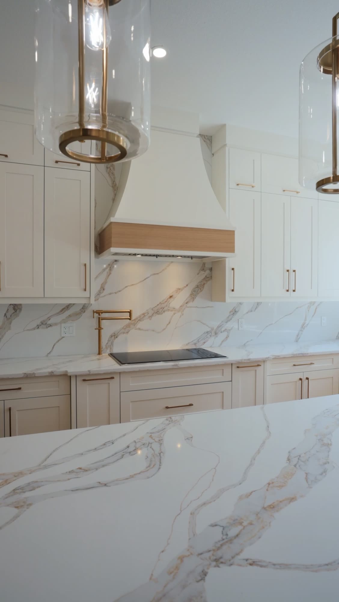 Kitchen with a marble backsplash, brass pendants and an oak banded hood